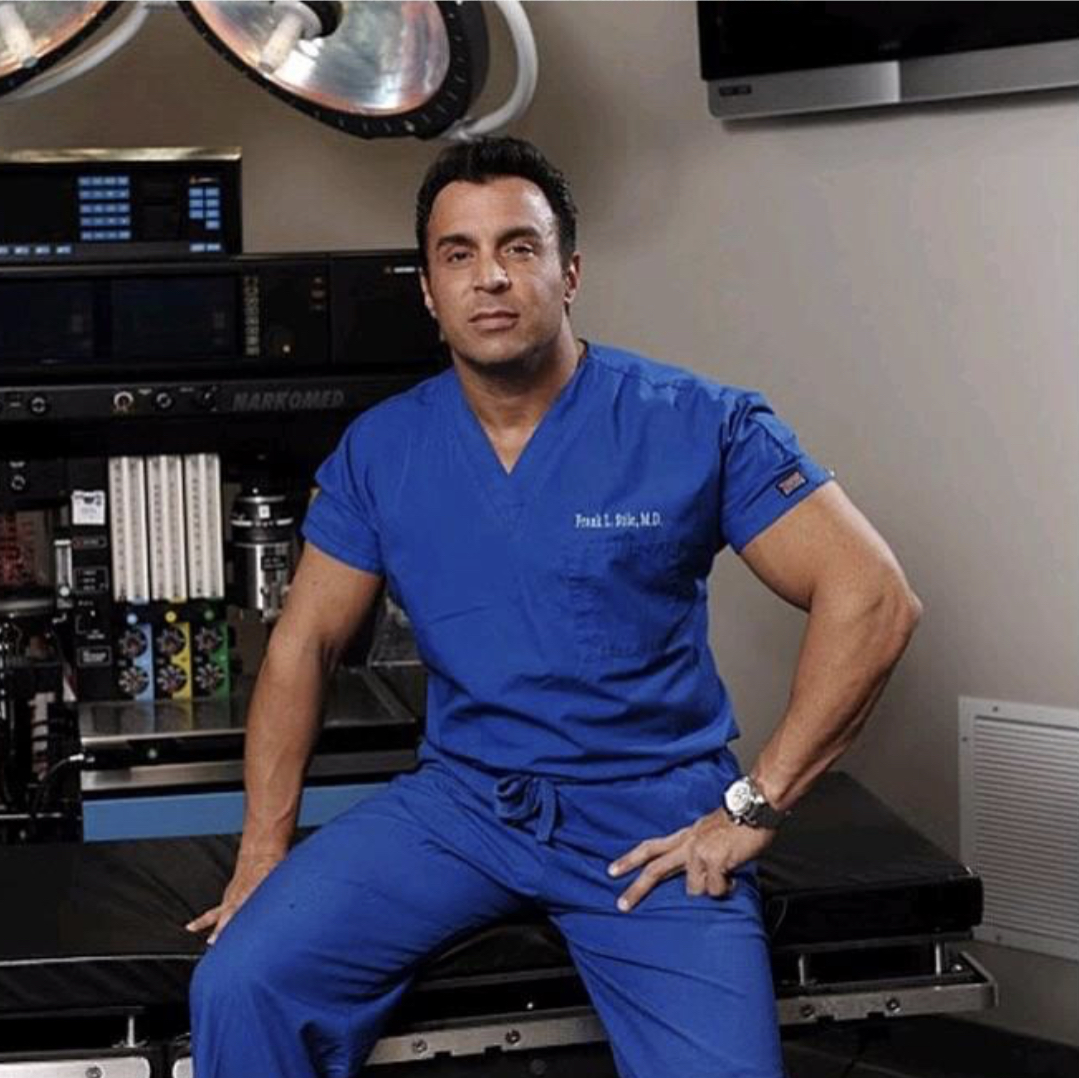 Dr. Stile in Scrubs Sitting on Desk